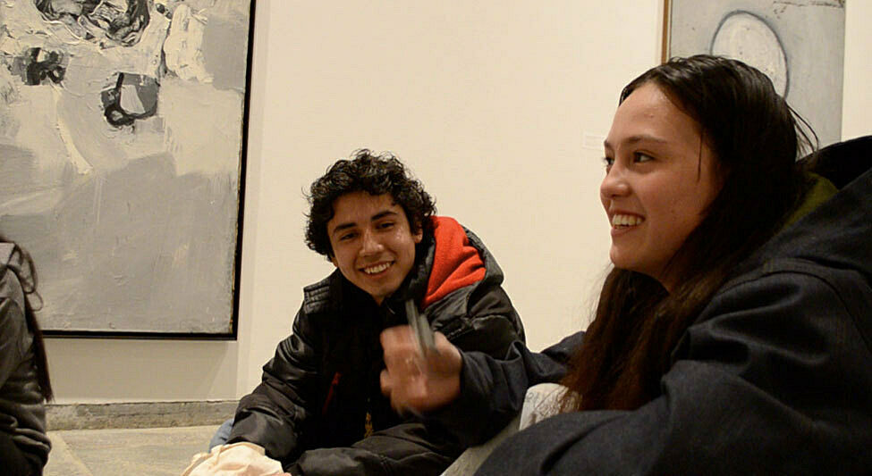 Two students smile as they discuss art in a gallery.