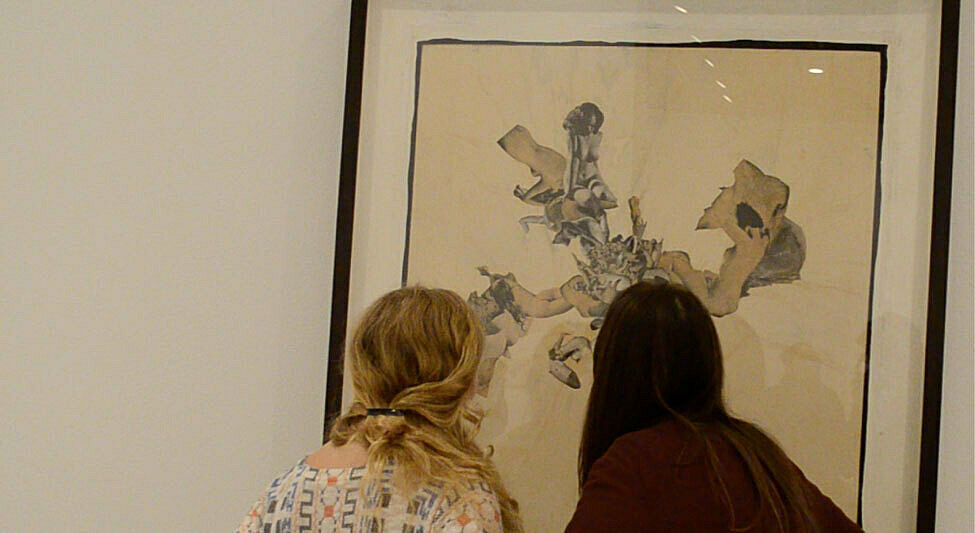 The back of two students heads as they examine a painting up close. 