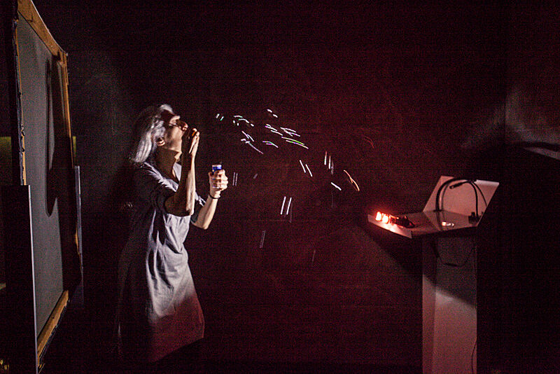 A woman blows bubbles in a darkened gallery.