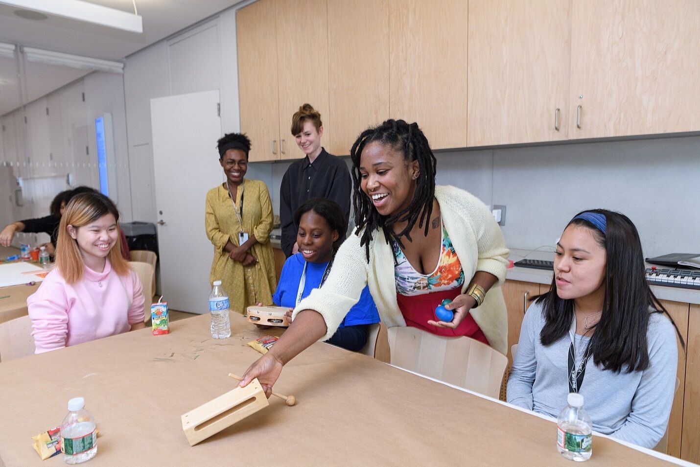 The artist places a wooden box on a table as students and staff members look on.