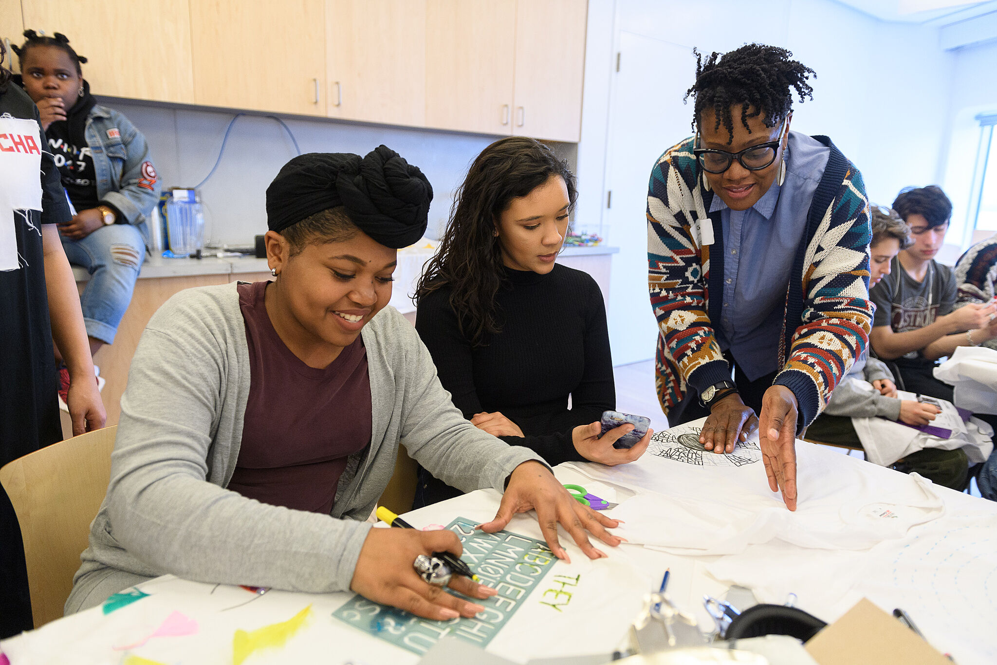 Teens work on an art project at a table and get input from a Biennial artist.