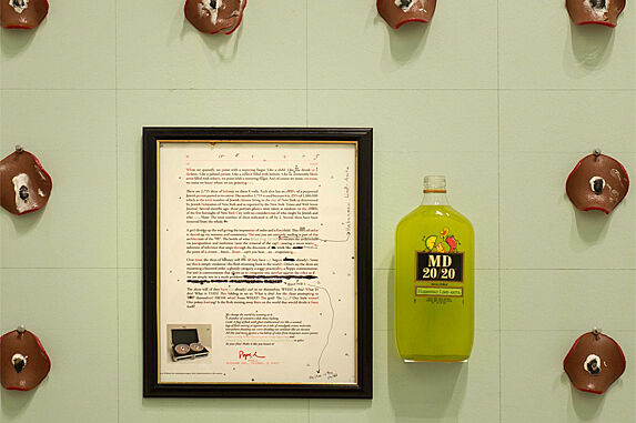 Grid-like structure of objects hung on wall with framed document and liquor bottle