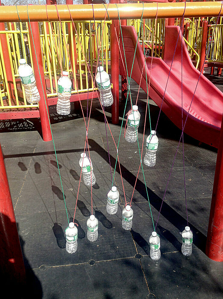 Artwork featuring water bottles hanging from string in a playground.
