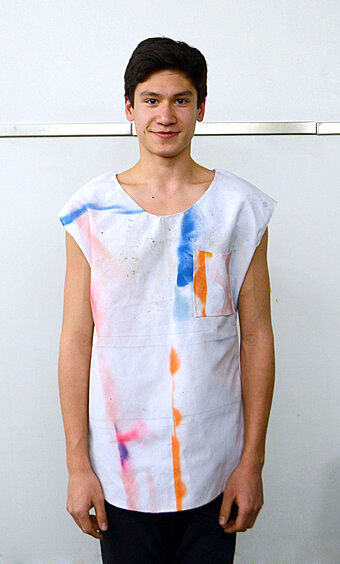 A teen artist wears a white shirt with blue and orange paint on it. 
