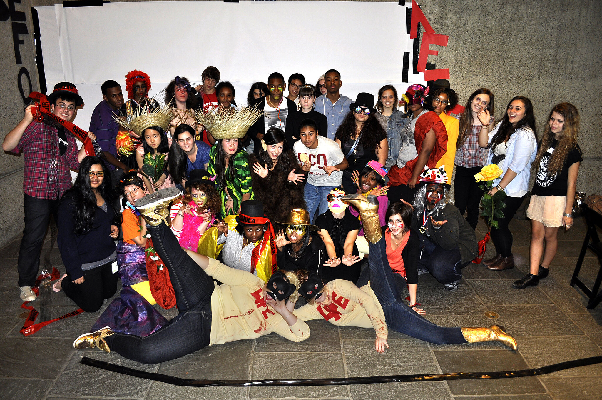 A large group of people in colorful costumes pose and make playful gestures for a group photo.