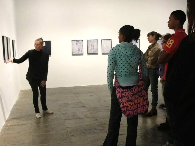 Sara VanDerBeek points to a painting in a gallery while students look on.