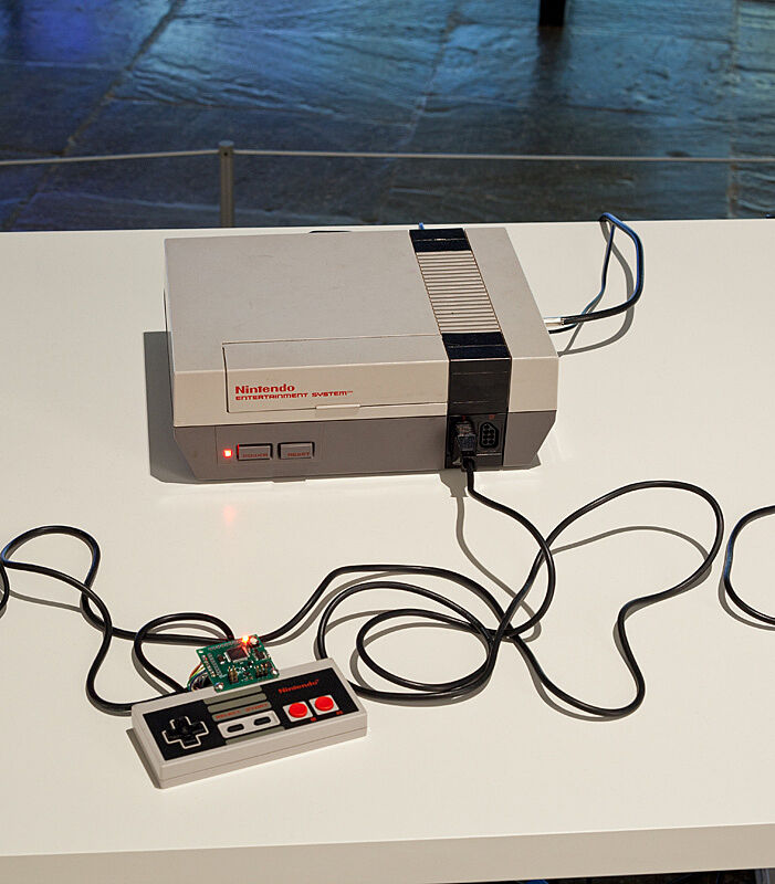 Installation view of Various Self Playing Bowling Games (aka Beat the Champ) by Cort Arcangel. Image depicts vintage Ninetendo game system and controllers. 