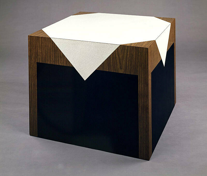 Laminate image of a wooden table and a white table cloth printed on a plywood cube sculpture. 