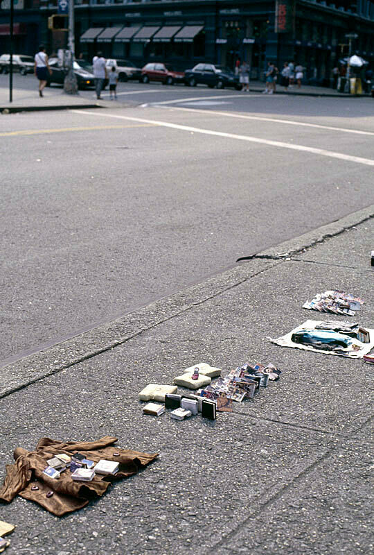Installation view of Charles Ledray's workworkworkworkwork exhibition at New York's Astor Place. Photograph depicts an array of clothing, books, pottery and other personal relics displayed on the sidewalk.