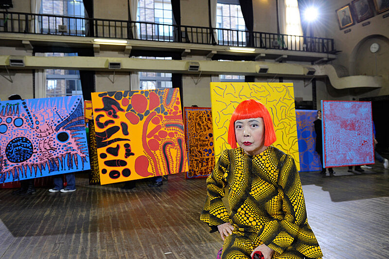 Photograph of a woman in front of paintings.