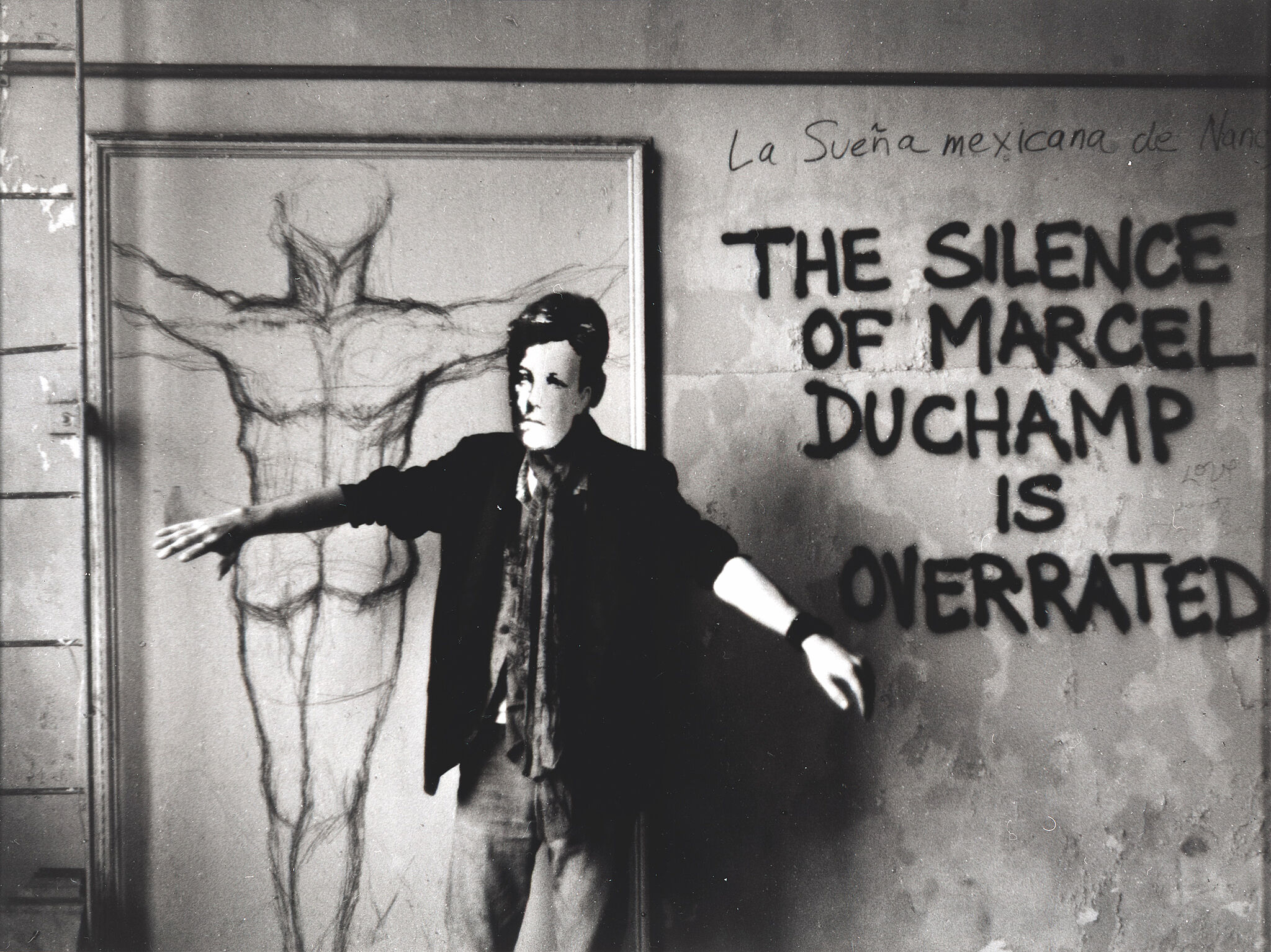 A man in an Arthur Rimbaud masking standing in front of graffiti. 