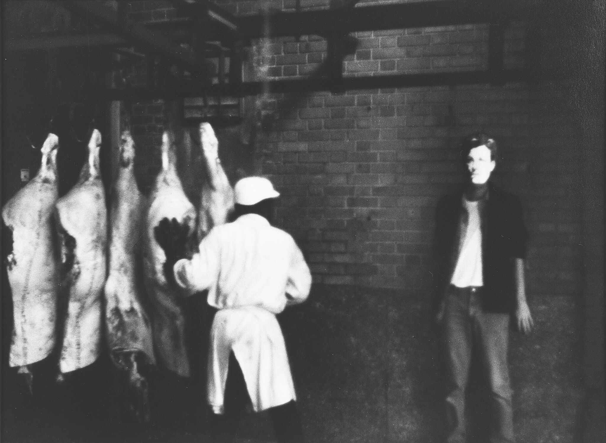 Man with Arthur Rimbaud mask standing in a meat packing factory. 
