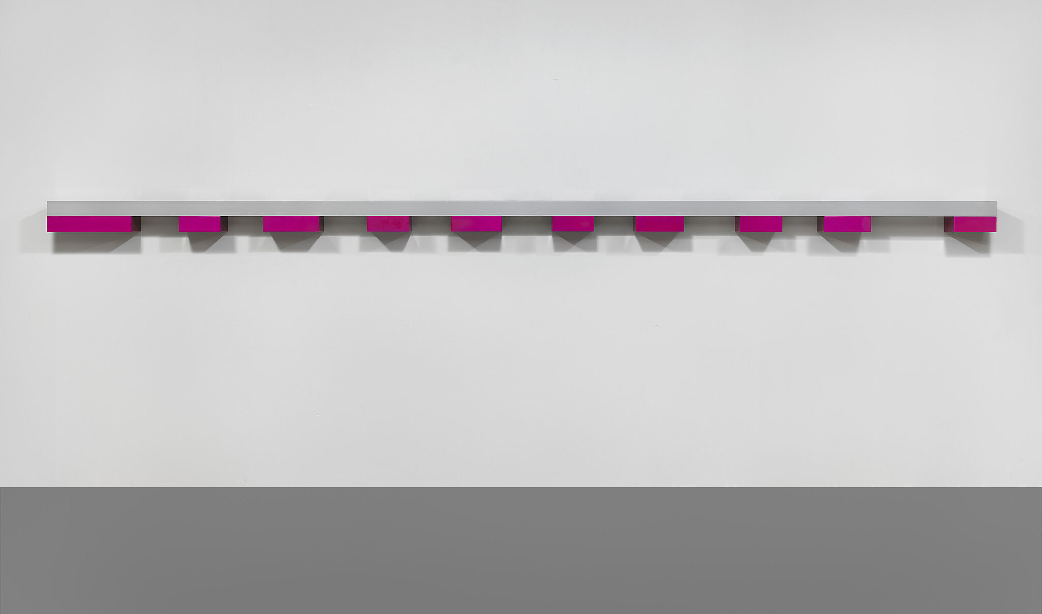 A horizontal sculpture made of pink metal boxes hanging on a wall.