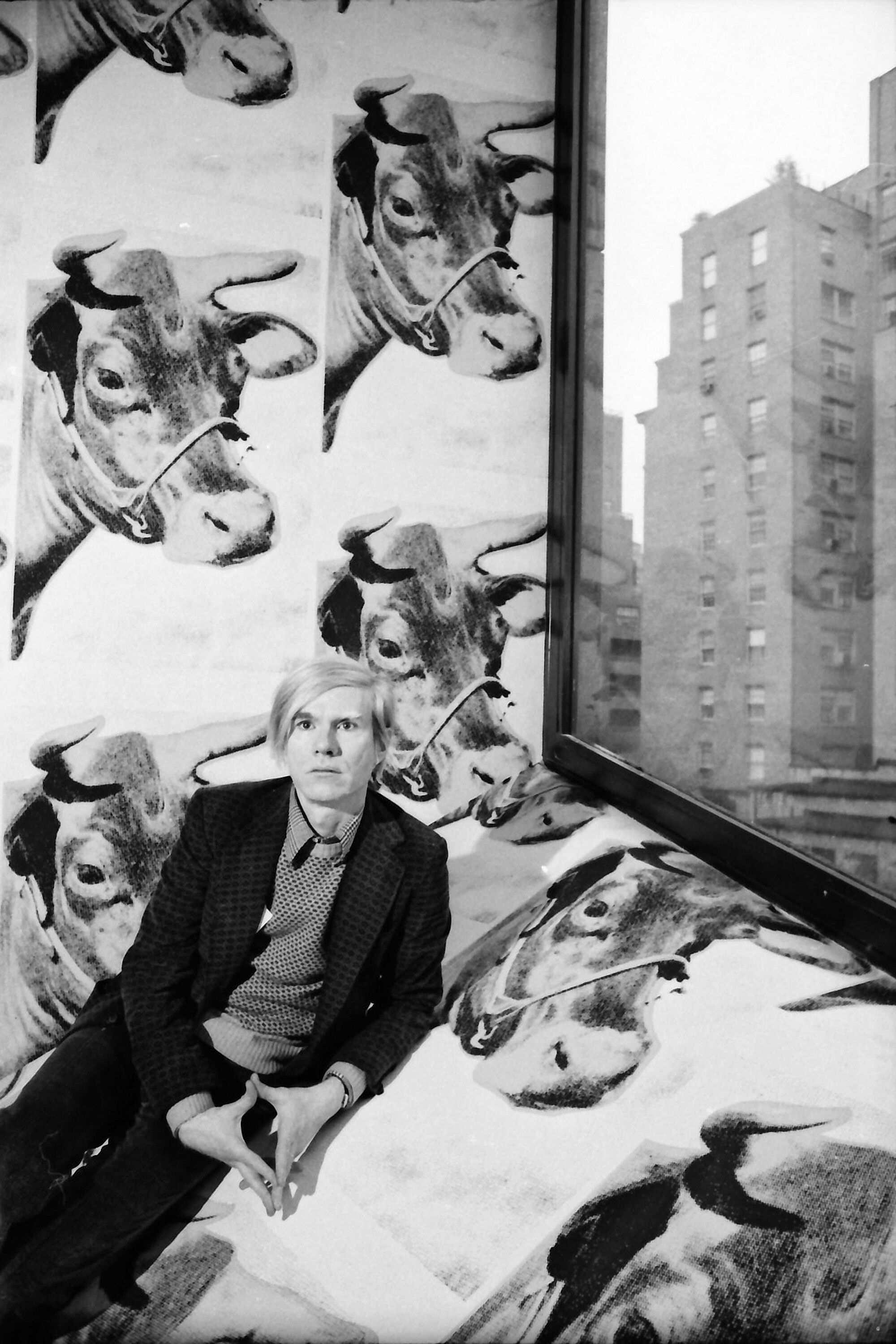 A portrait of Andy Warhol sitting in front of a window