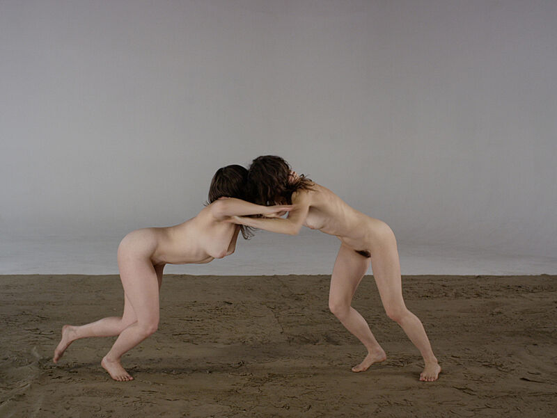 Two naked women pushing each other. 
