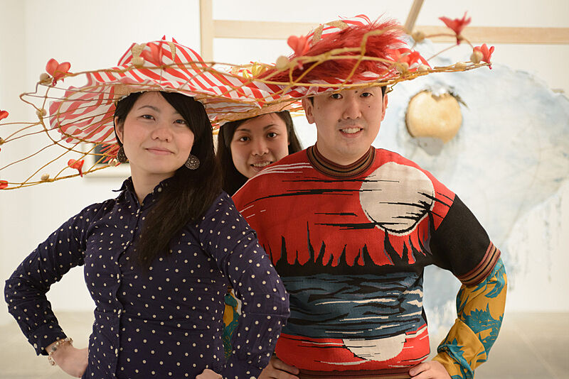 Three people wearing flower decorated hats. 