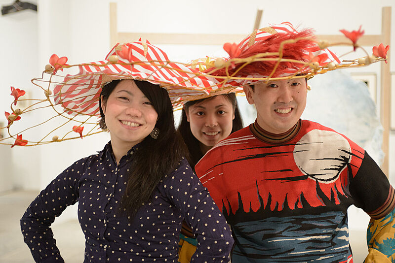 Three people wearing flower decorated hats. 