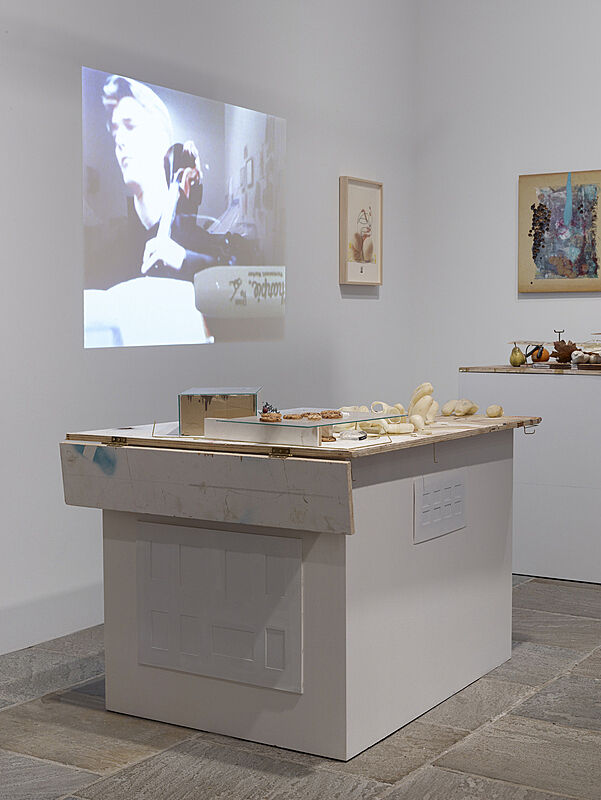 Installation view of a video projected on the wall and artworks on table. 