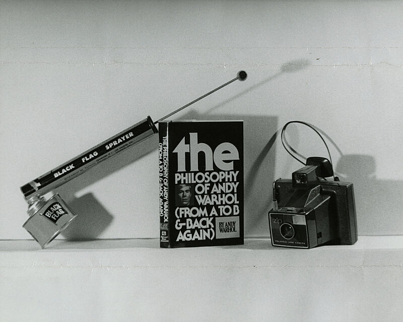 A photograph of a black flag sprayer, a vintage camera and a book in the middle. 