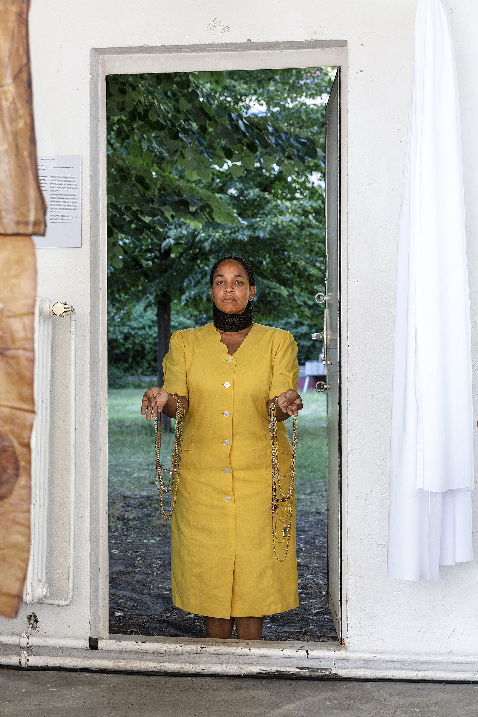 A view of a woman in a yellow dress standing in a doorway that leads to a yard.