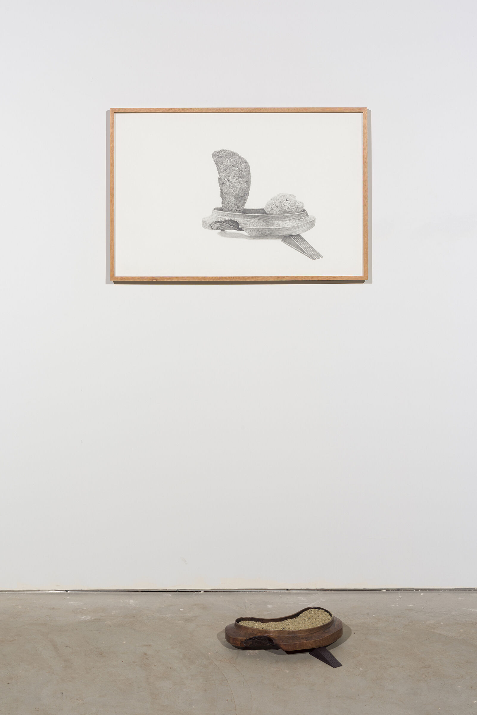An installation including a black-and-white drawing on the wall and small sculpture on the ground before it.