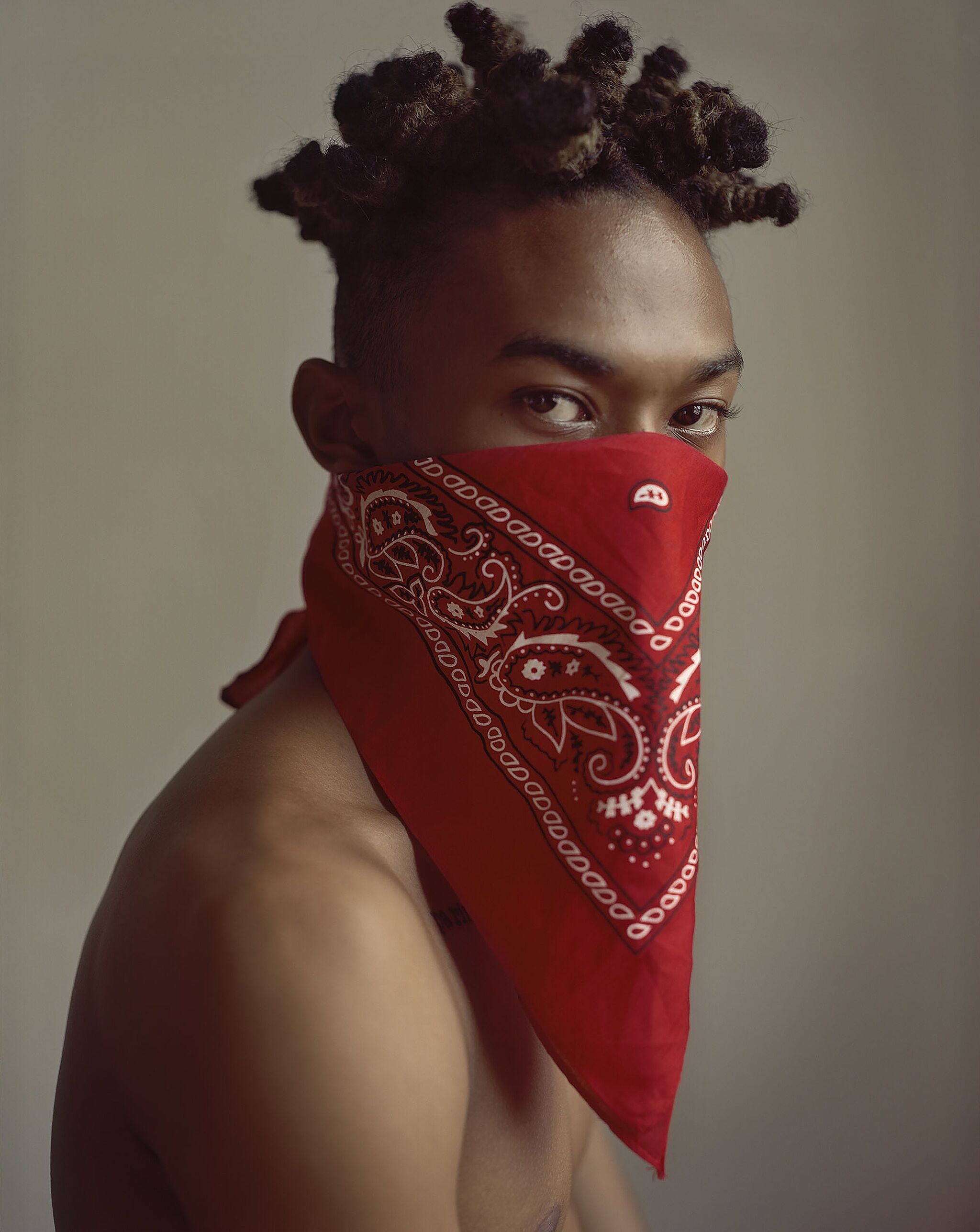 A photograph of a person from the shoulders up wearing a red bandana around the lower half of their face.