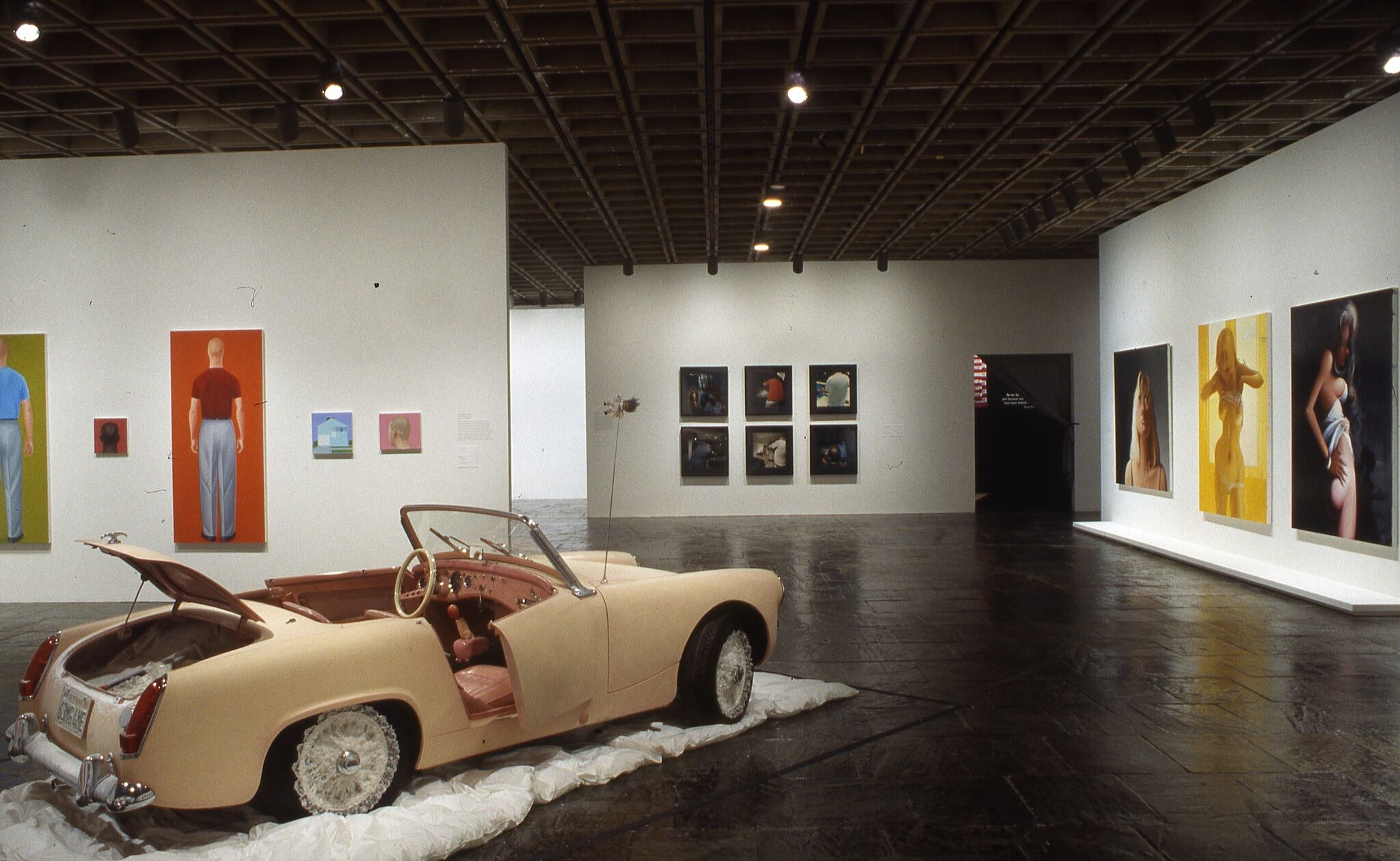 A gallery filled with works of art on the walls and a sculpture of a car.