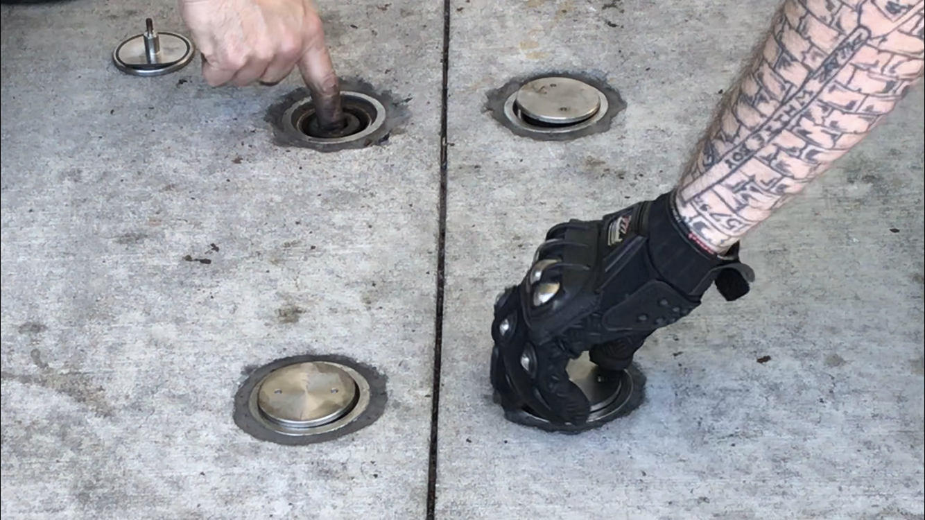 A hand placing a metal disk on a concrete panel.