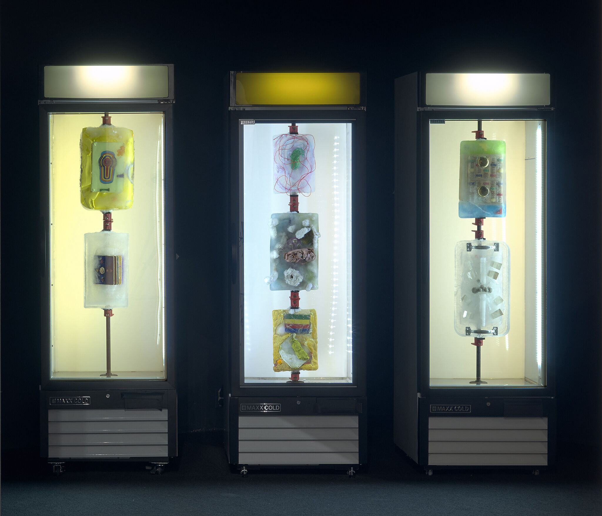 An installation view of three freezers with materials frozen inside.