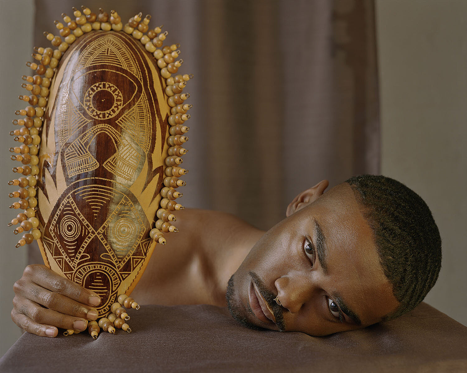 A man lying down and looking at the camera holding a fan.