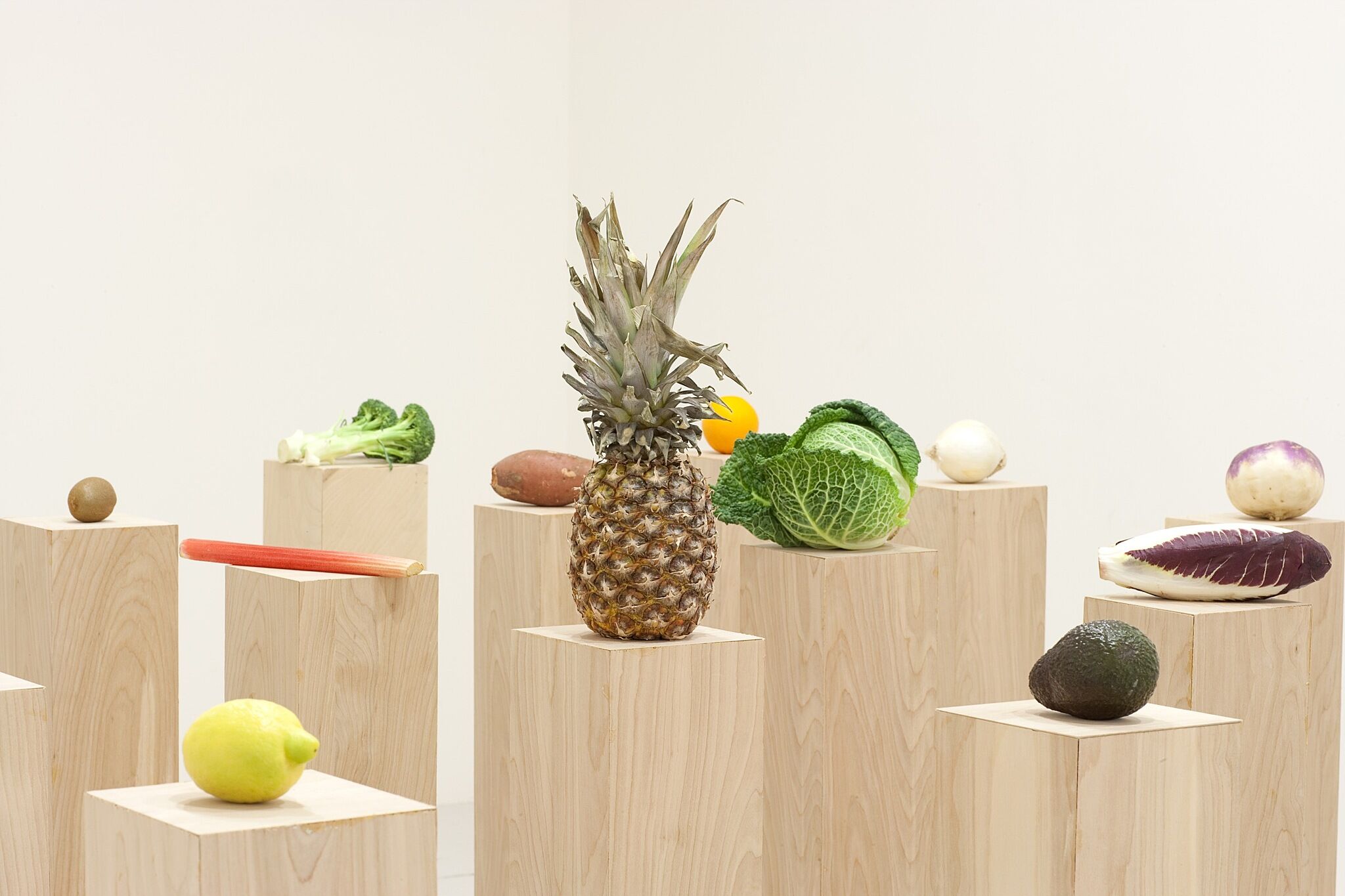 A photo of various fruits and vegetables perched on wood plinths