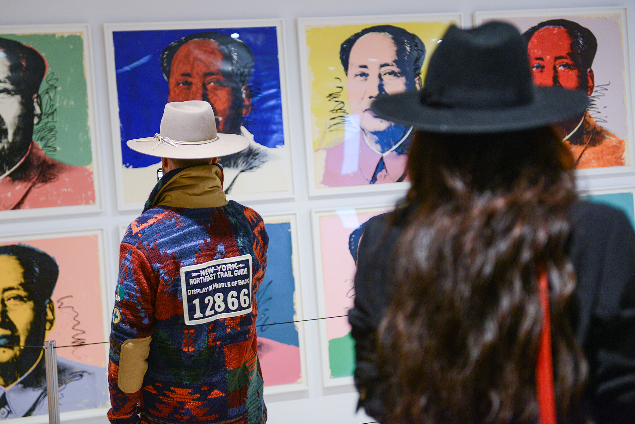 Two people observing colorful Warhol-style portraits in an art gallery.