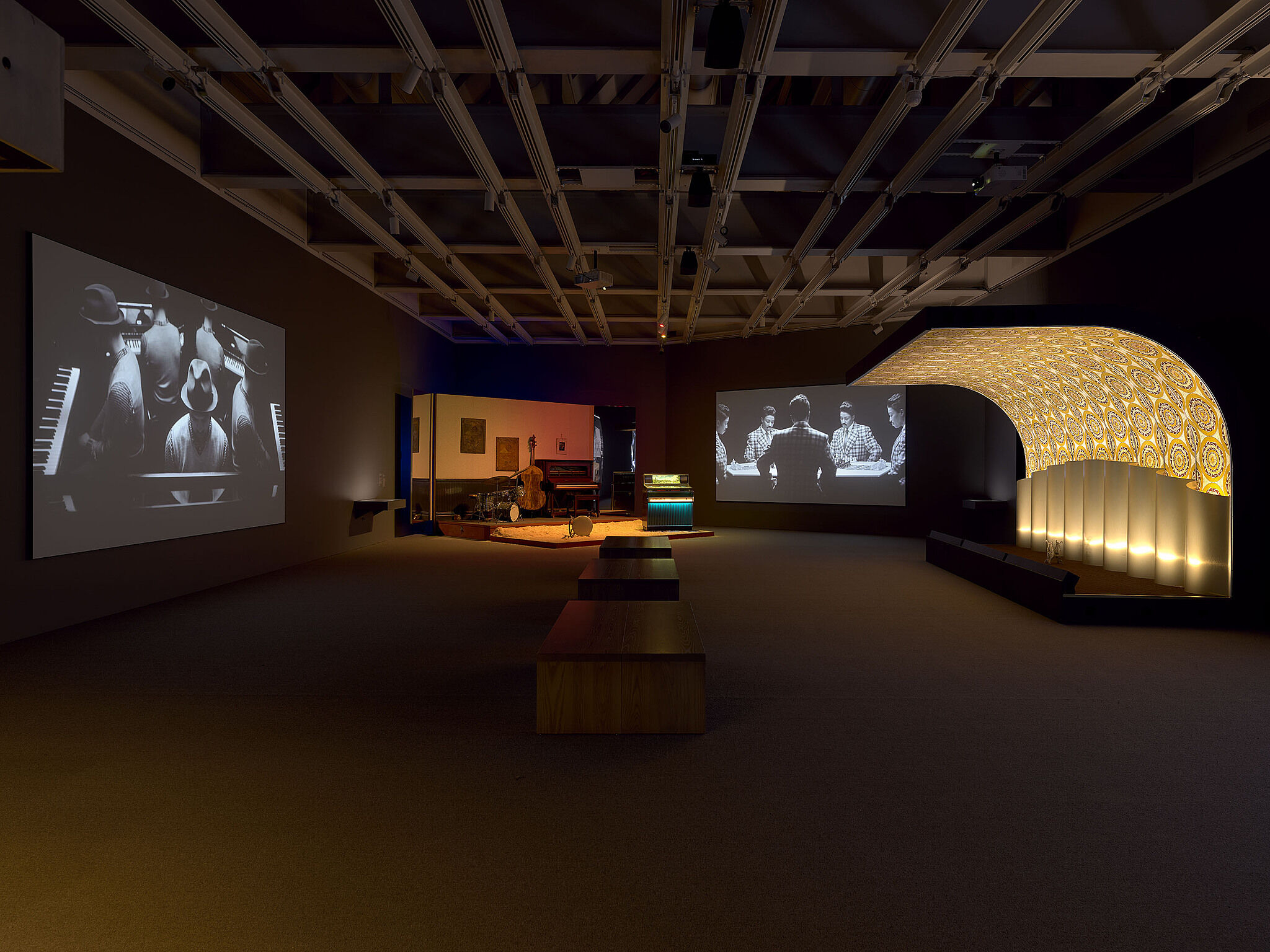 An image of a gallery with three stages and various musical instruments and video projections.