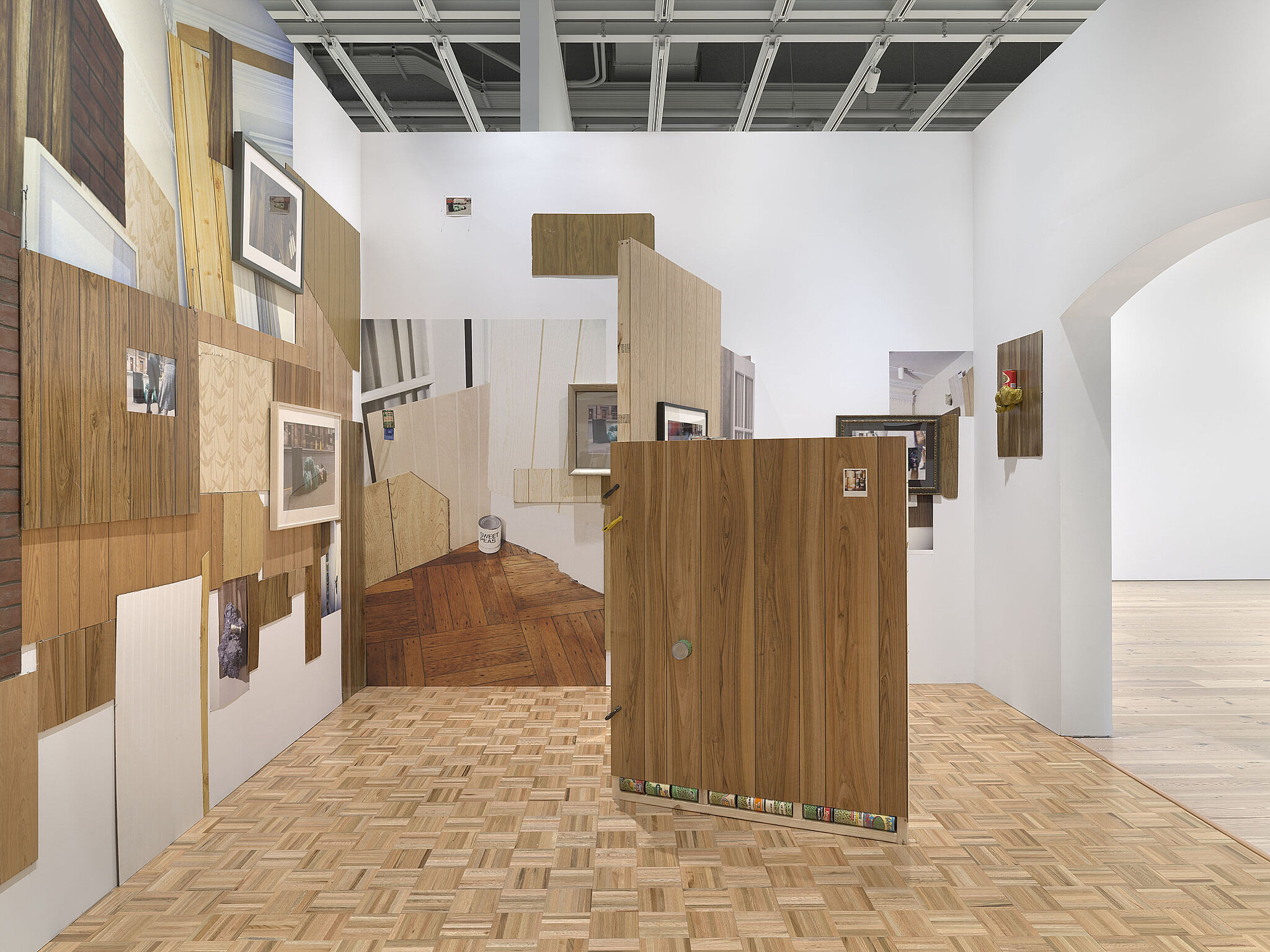 A gallery with fake wood walls, large photographs, and cans of peas.