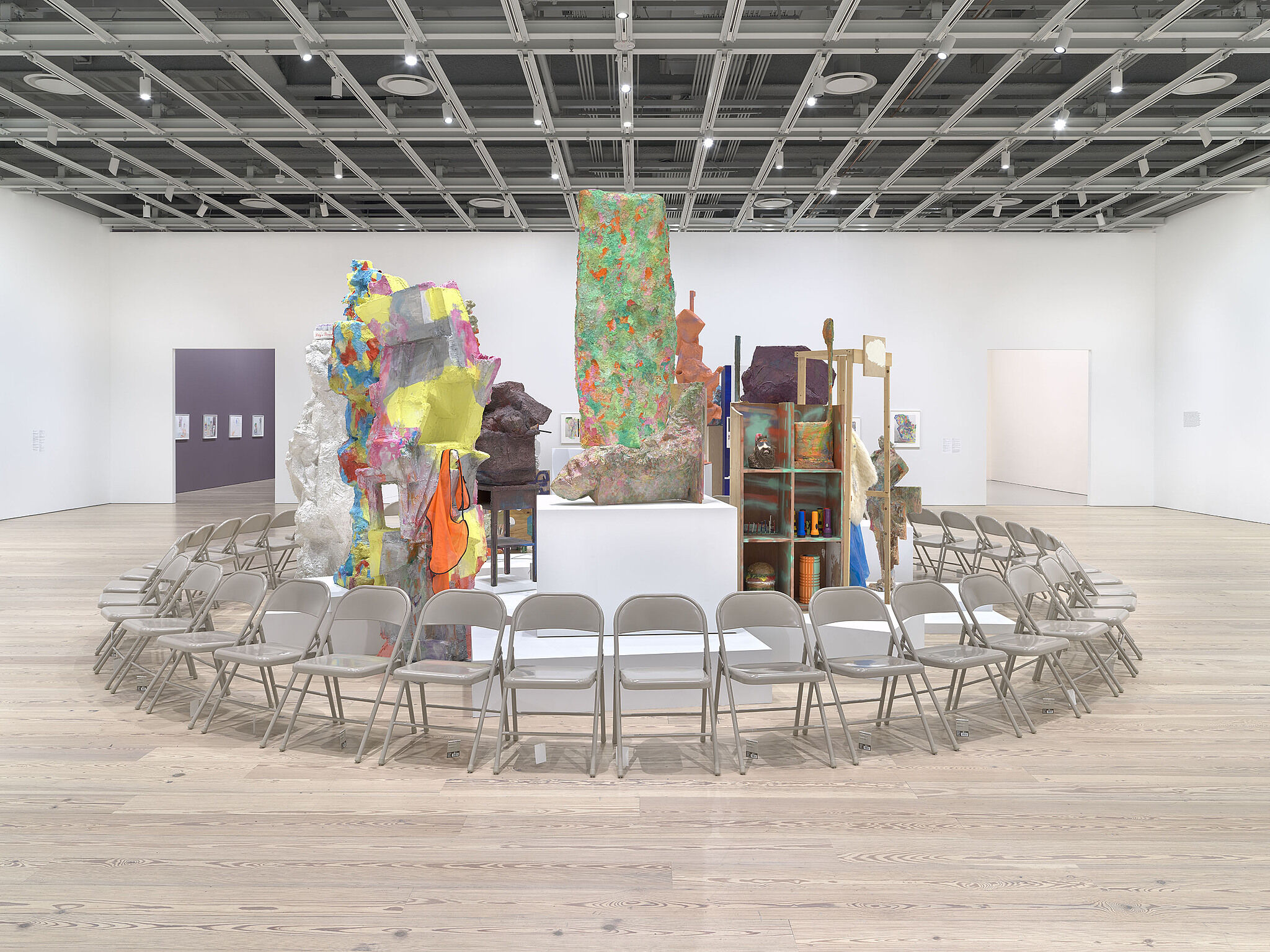 A ring of chairs surround various sculptures in a gallery.