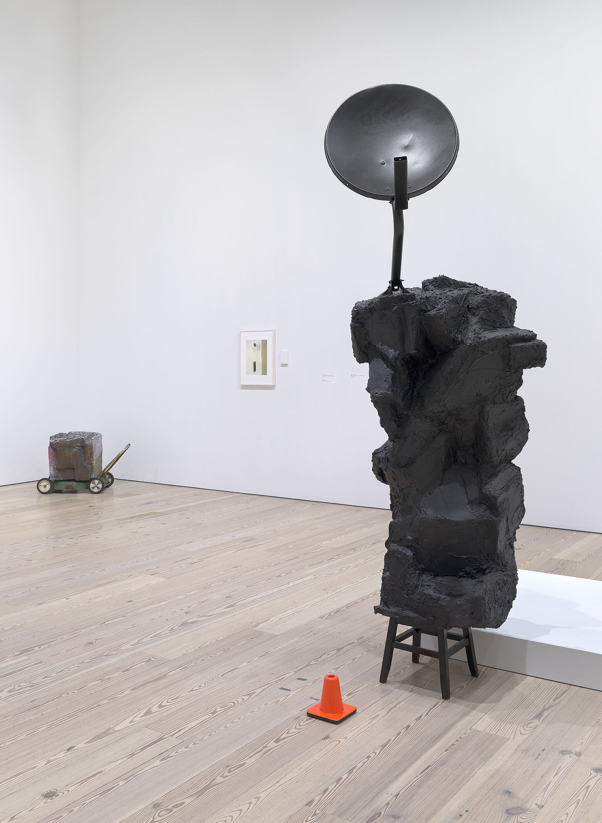 A sculpture with a black satellite dish, a black blob, and an orange caution cone.