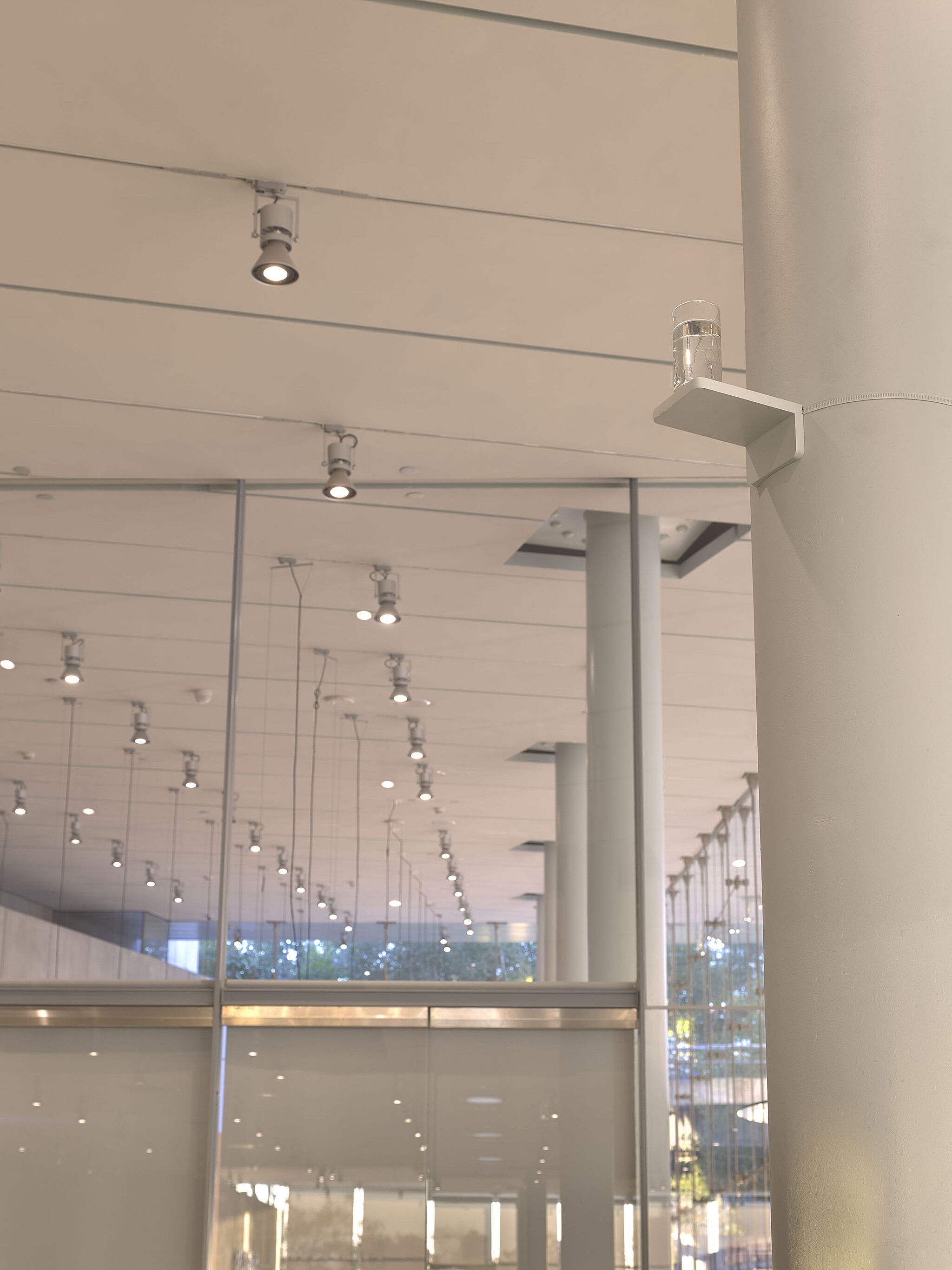 A glass of water sitting on a high shelf in the Whitney lobby.