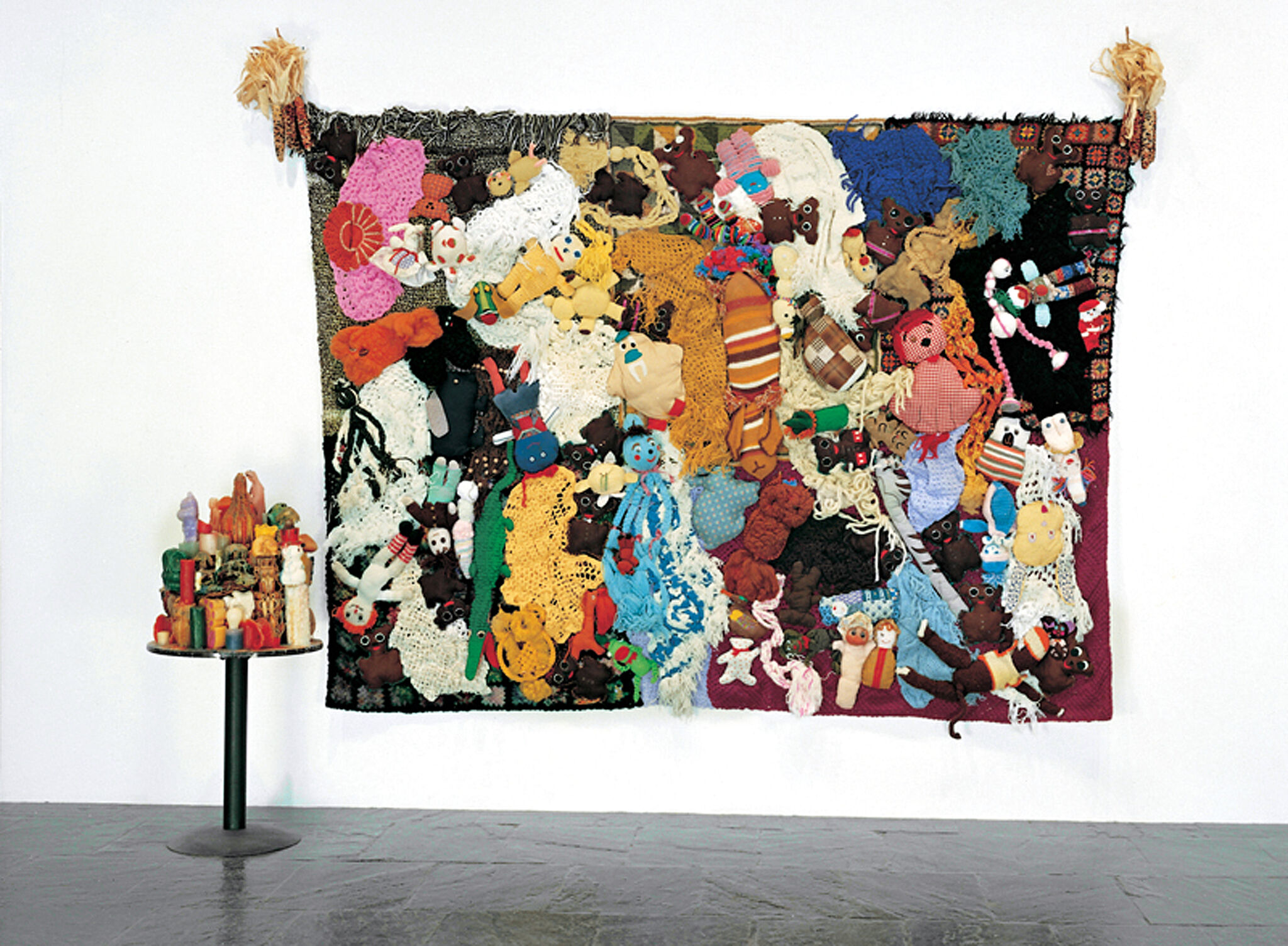 A wall with a sculpture made of stuffed animals and a table with a sculpture made of wax candles.