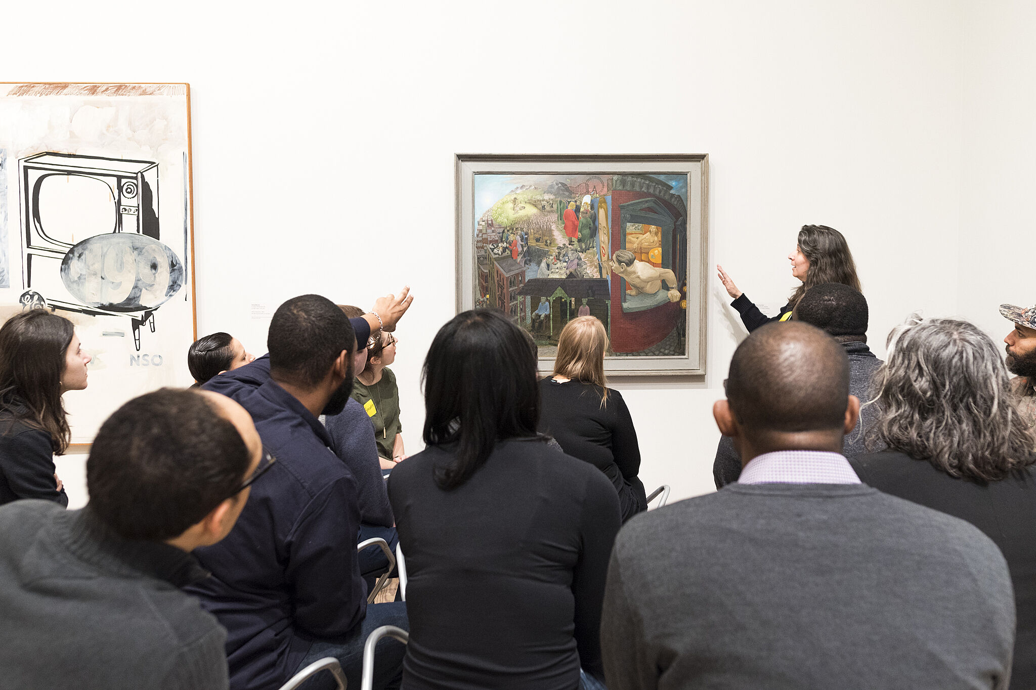 A photo of a woman pointing at a painting while a small group looks at the piece.