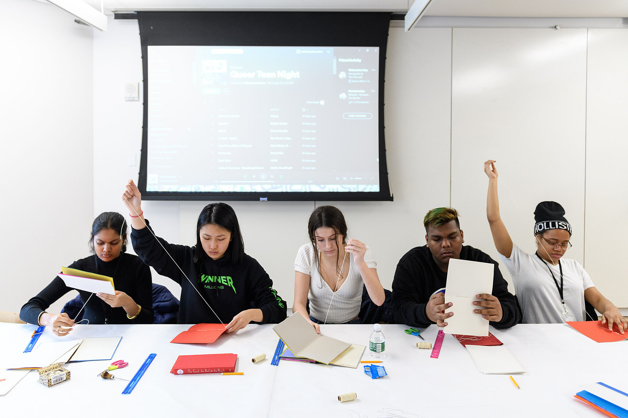 A photo of five teenagers sitting at a table making art.