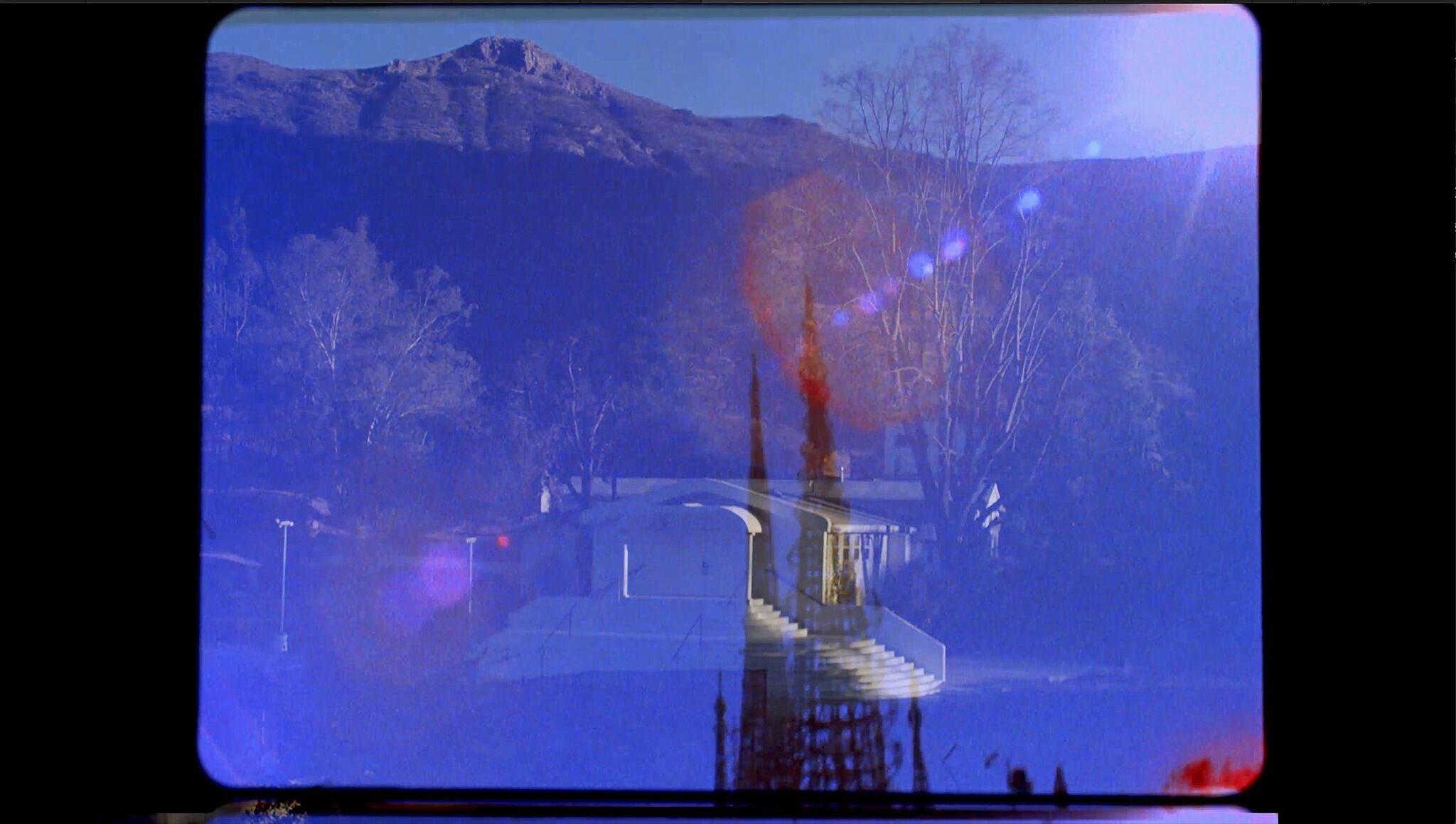 A film still with overlapping images of a spire and mountains.