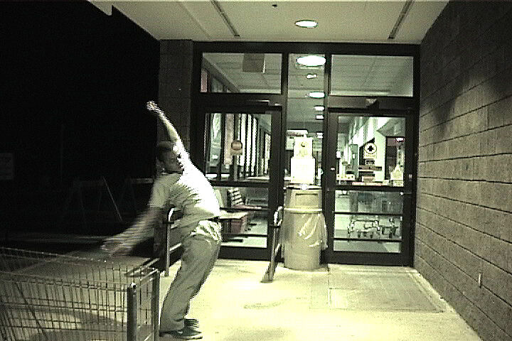 A grainy still of a man outside a supermarket with a shopping cart in view