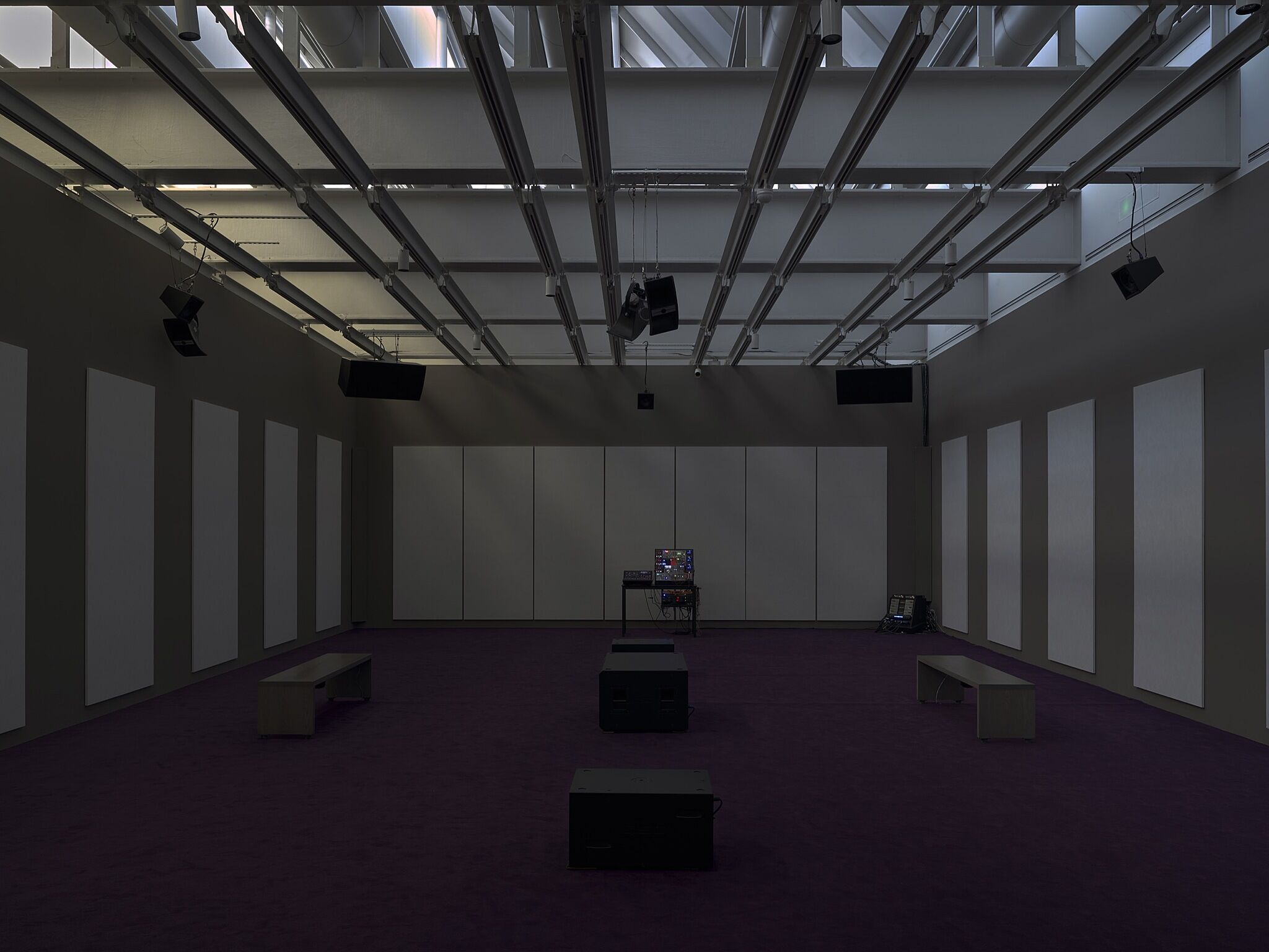 A dimly lit gallery space with speakers.