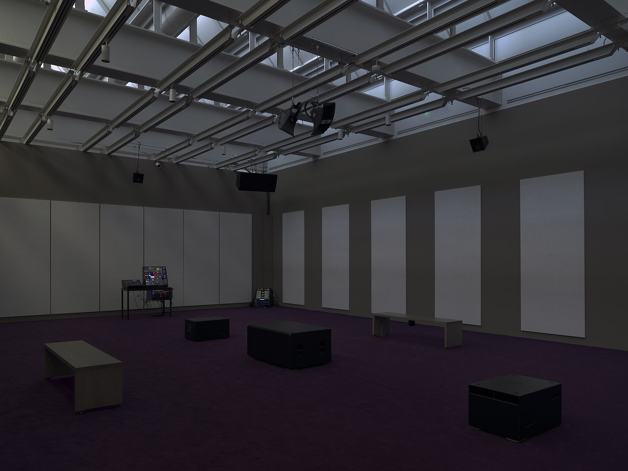 A dimly lit gallery space with speakers.
