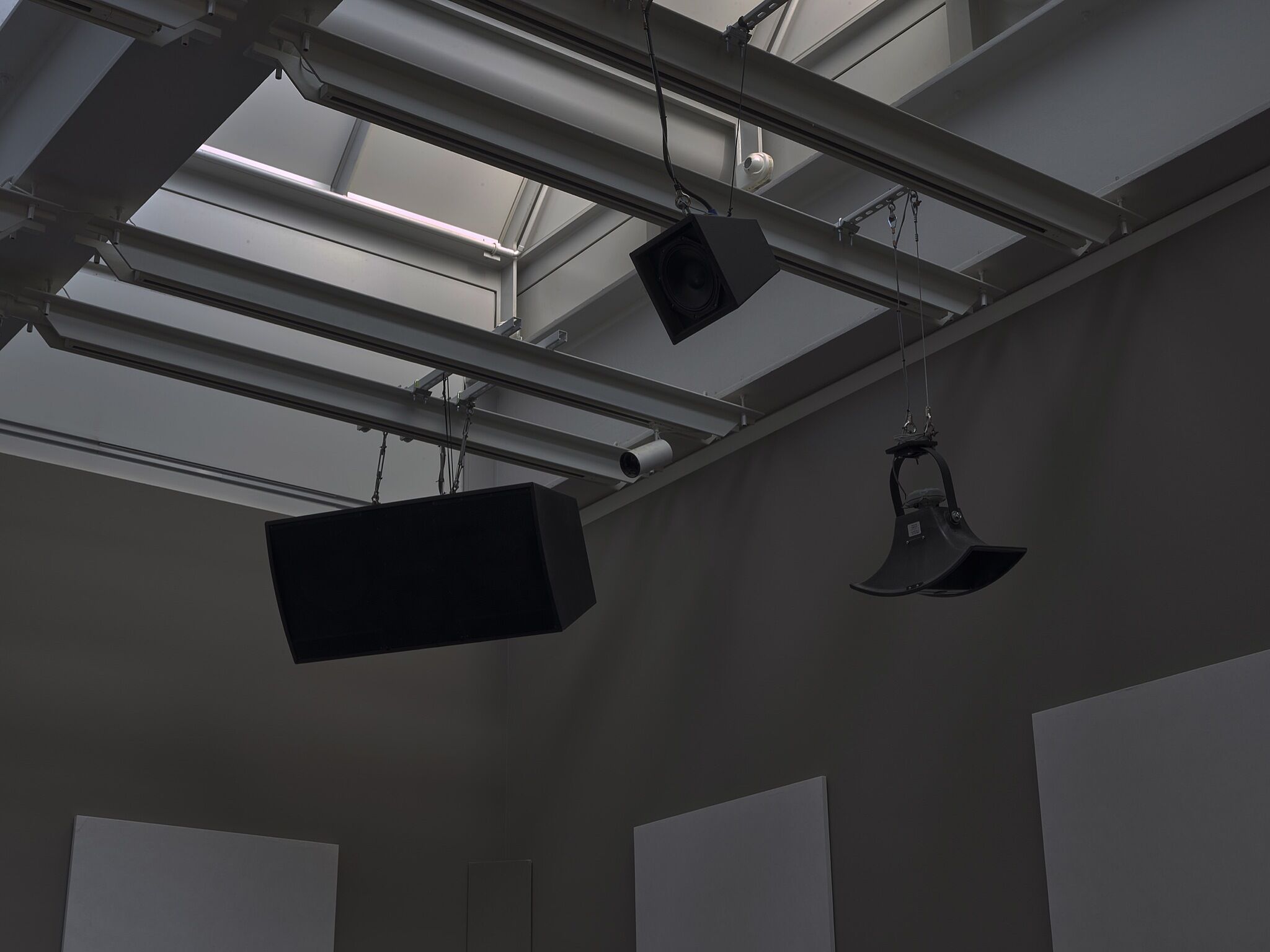 Speakers hanging from the ceiling of a dimly lit gallery.