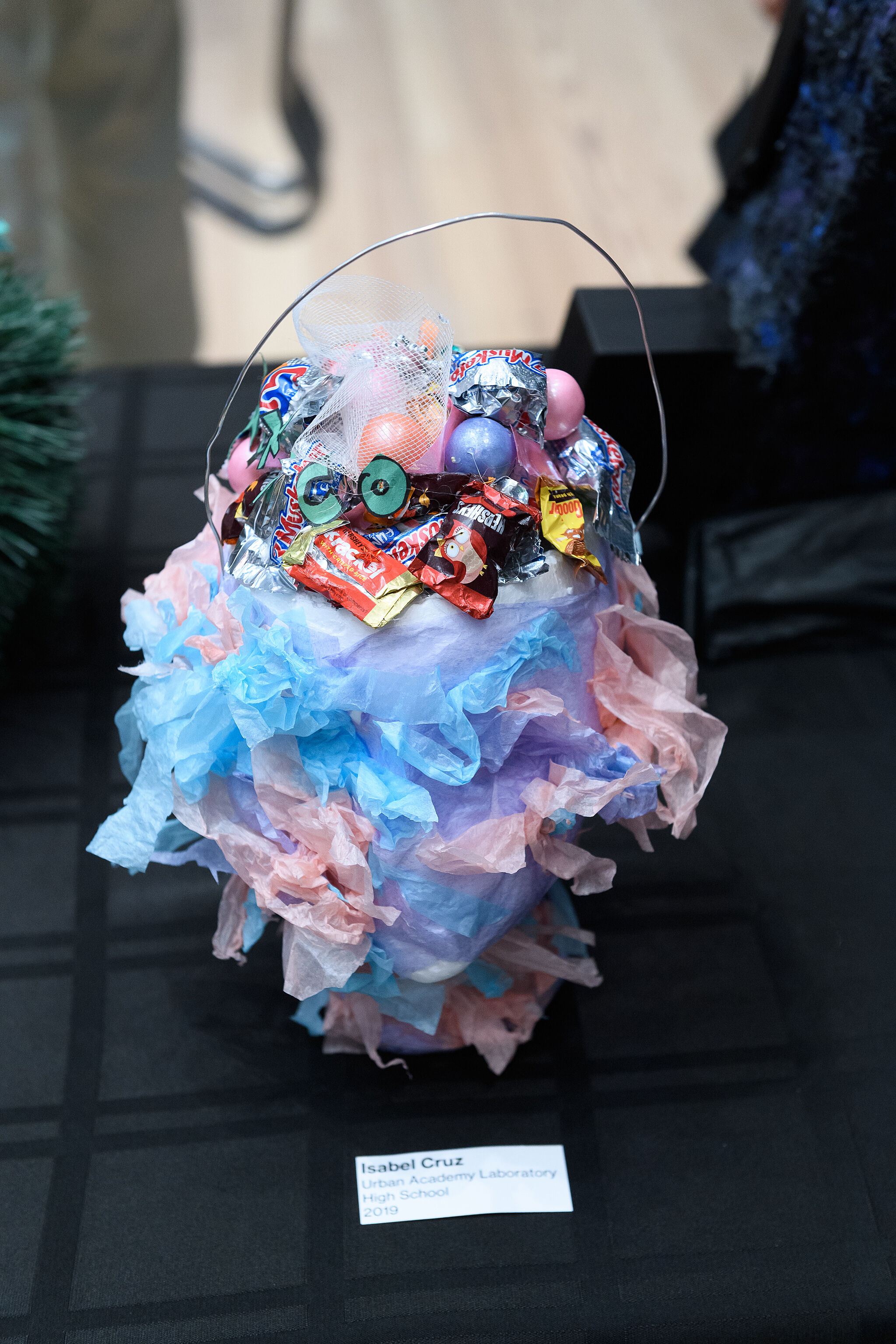 YI Artist, Isabel, displays her sculpture of a bucket wrapped in tissue paper and filled with candy wrappers, spring 2019