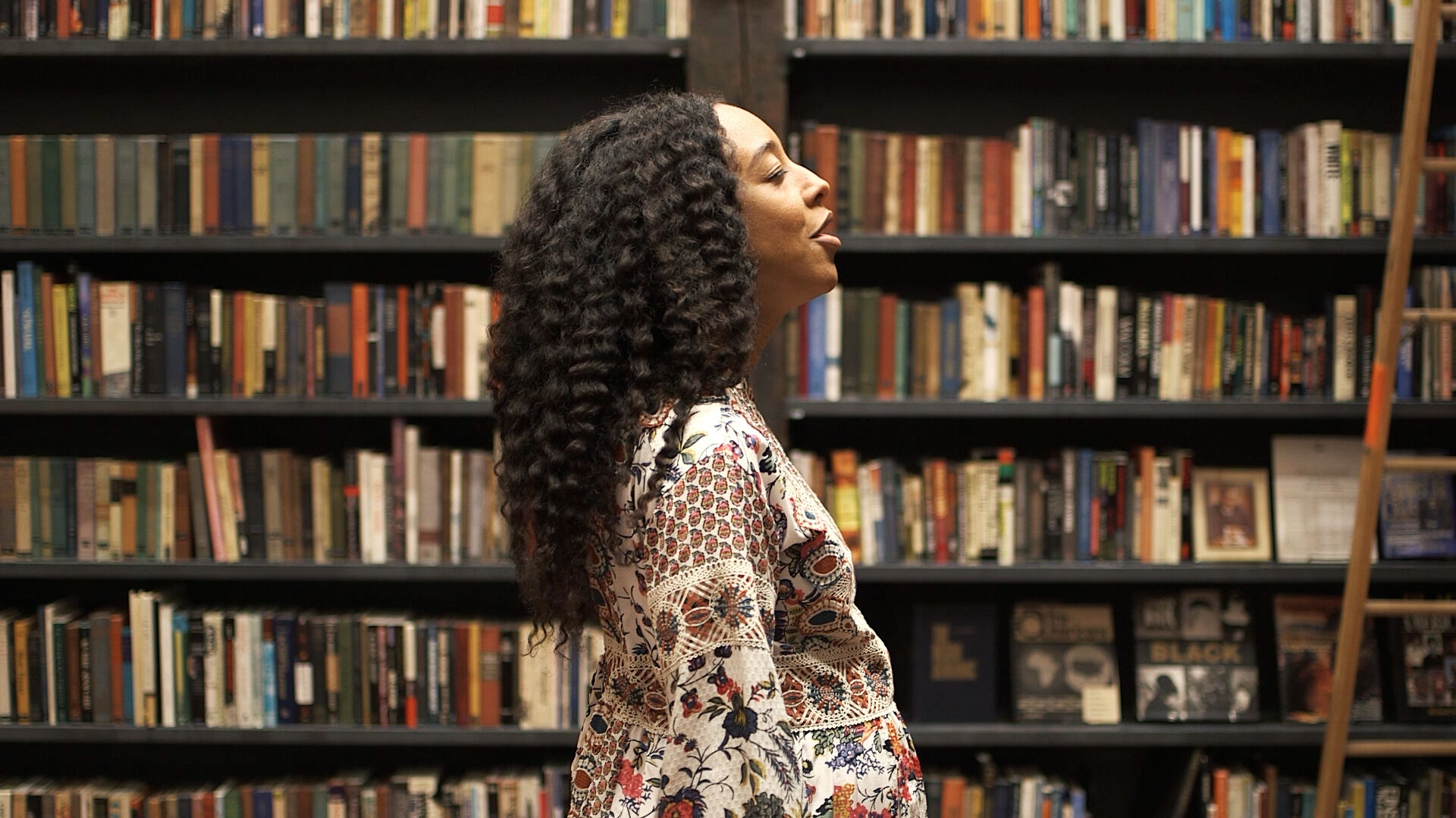A woman in profile view standing in front of a bookshelf.