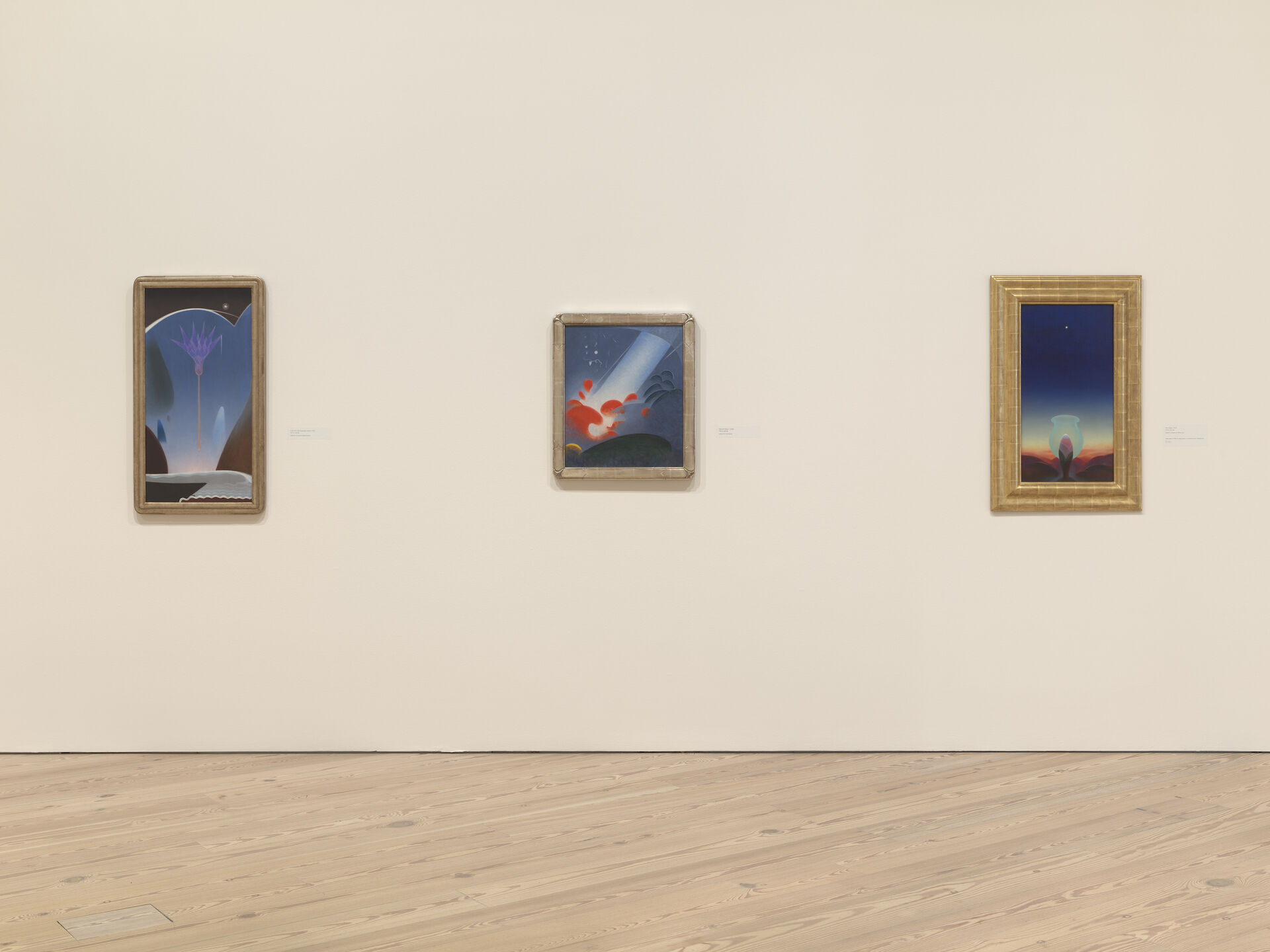 Three paintings appear directly ahead on a white wall at the Whitney Museum of American Art. The paintings by Agnes Pelton, from left to right, are Lotus for Lida (Egyptian Dawn), 1930; Red and Blue, c. 1938; and Star Gazer, 1929. 