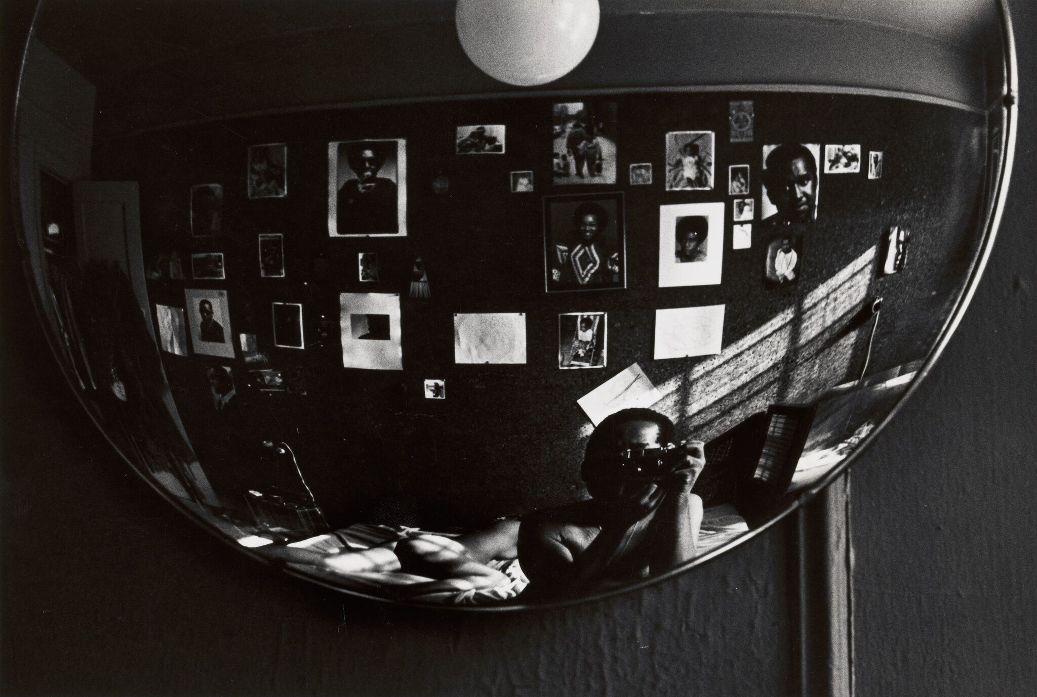 A reflection in a rounded mirror of a photographer and a wall of images.