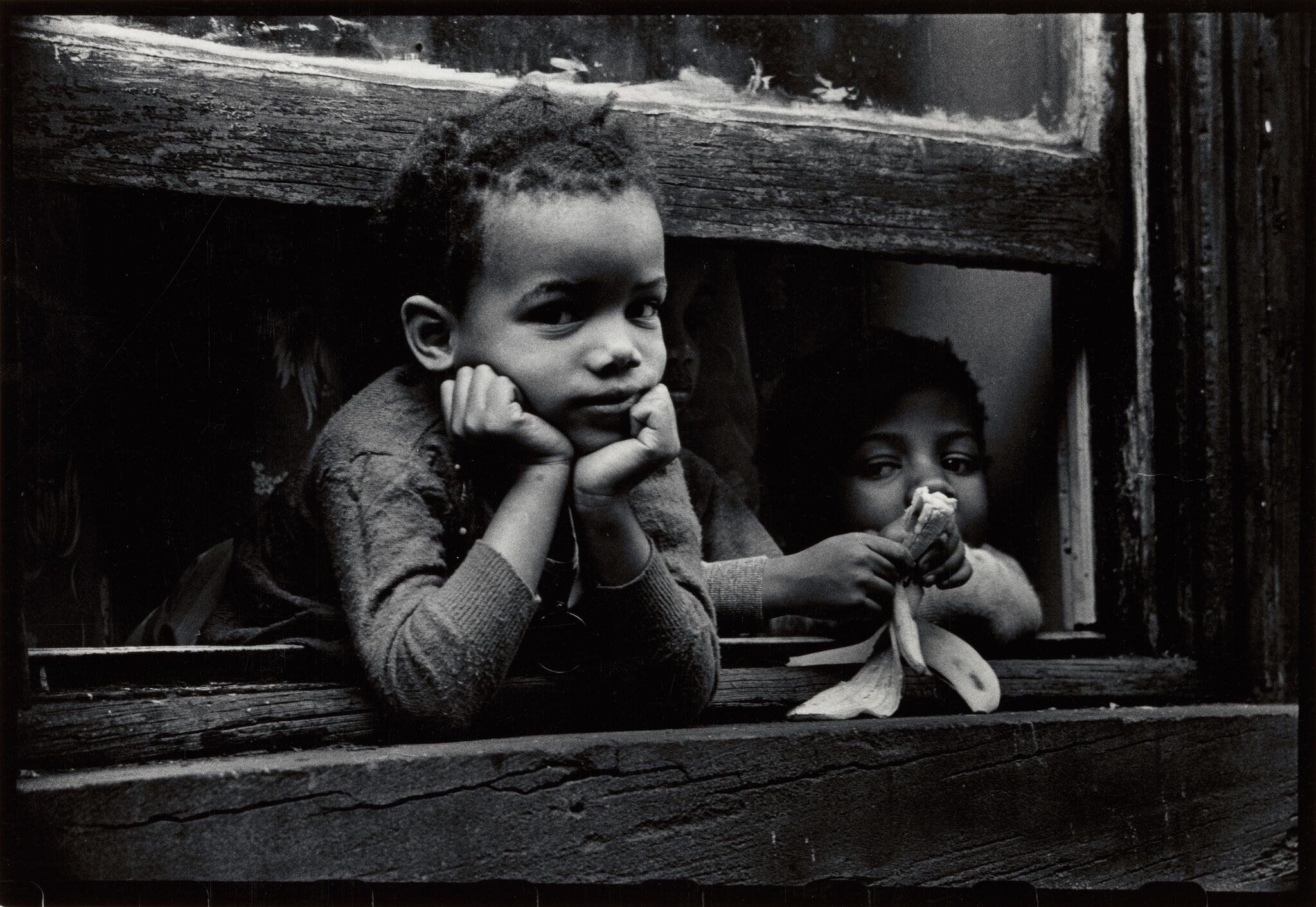 Two boys peeking out from a window.